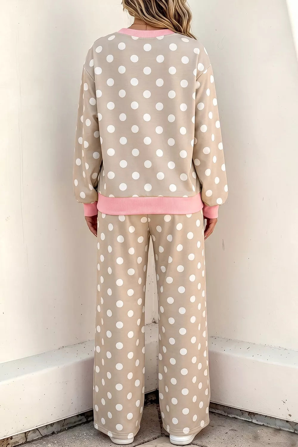 A person shown from the back wearing a beige and white polka dot lounge set with pink trim, standing against a plain off-white wall.