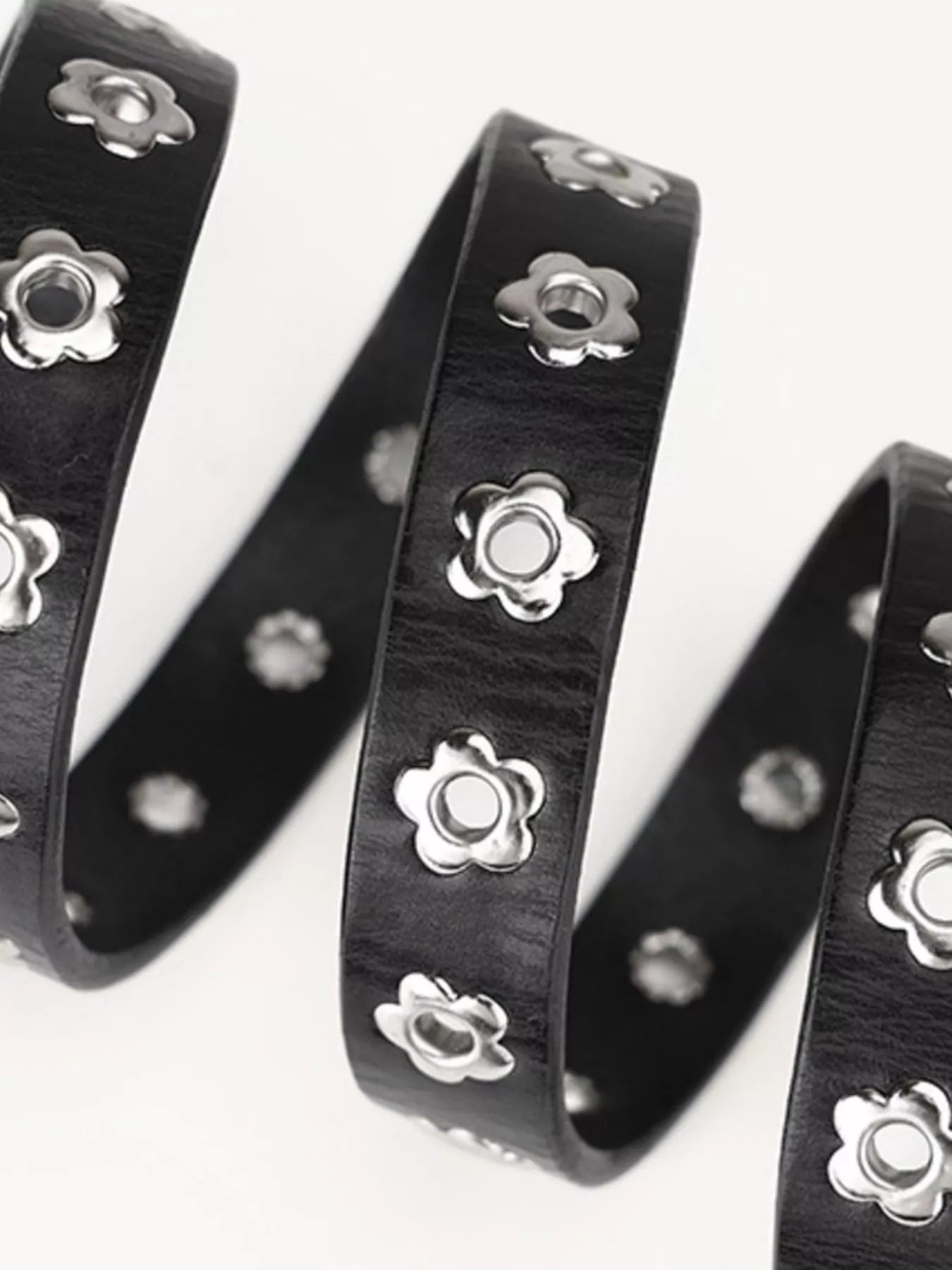 Black leather straps with silver floral metal studs on a white background