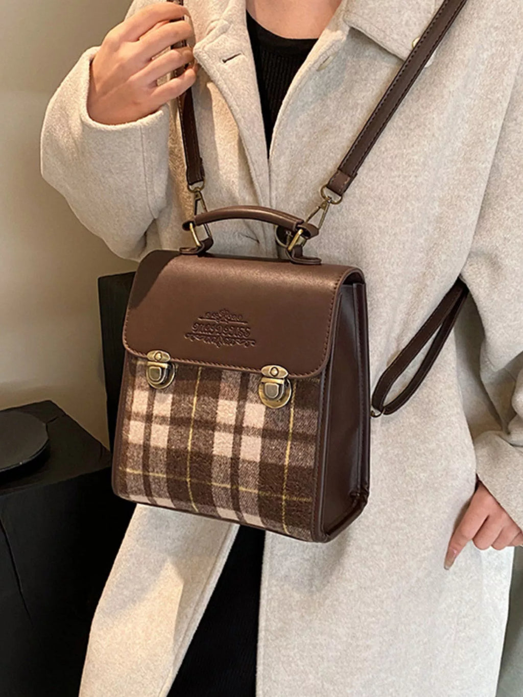 Model holding a brown and plaid backpack with a neutral background