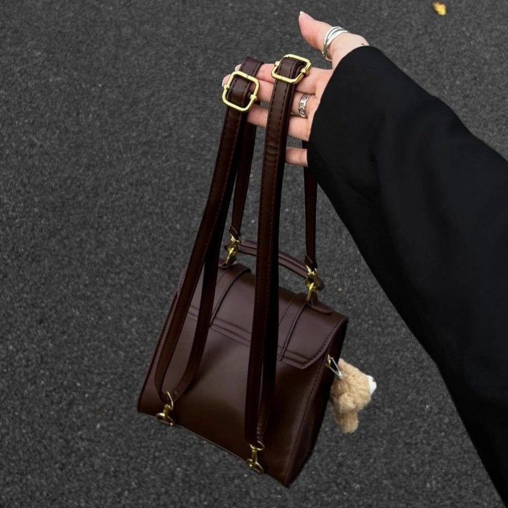 Brown handbag with gold accents held by a hand on a dark background