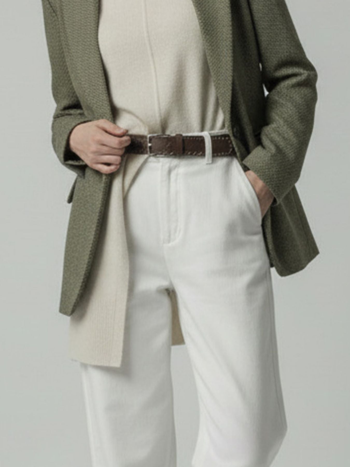 Model wearing a green blazer, beige sweater, and white pants on a plain background