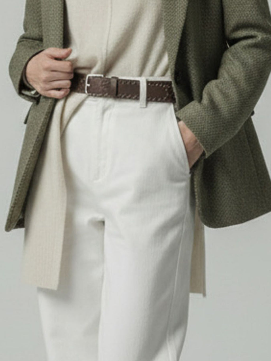 Model wearing a green blazer and white pants with a brown belt on a light gray background