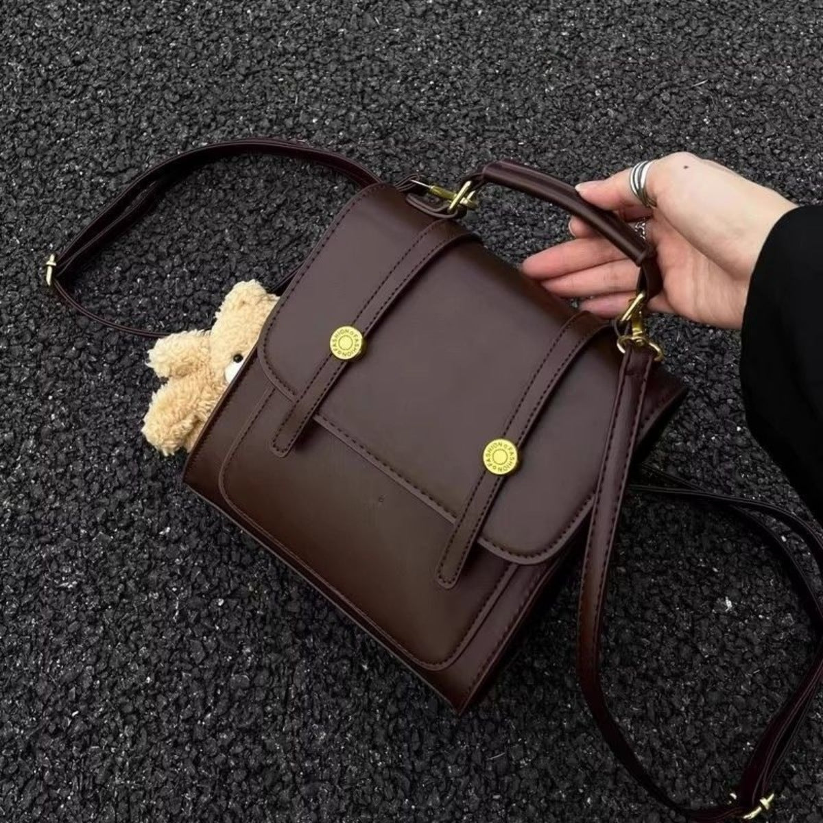 Brown handbag with gold buttons held by a hand on a dark textured surface