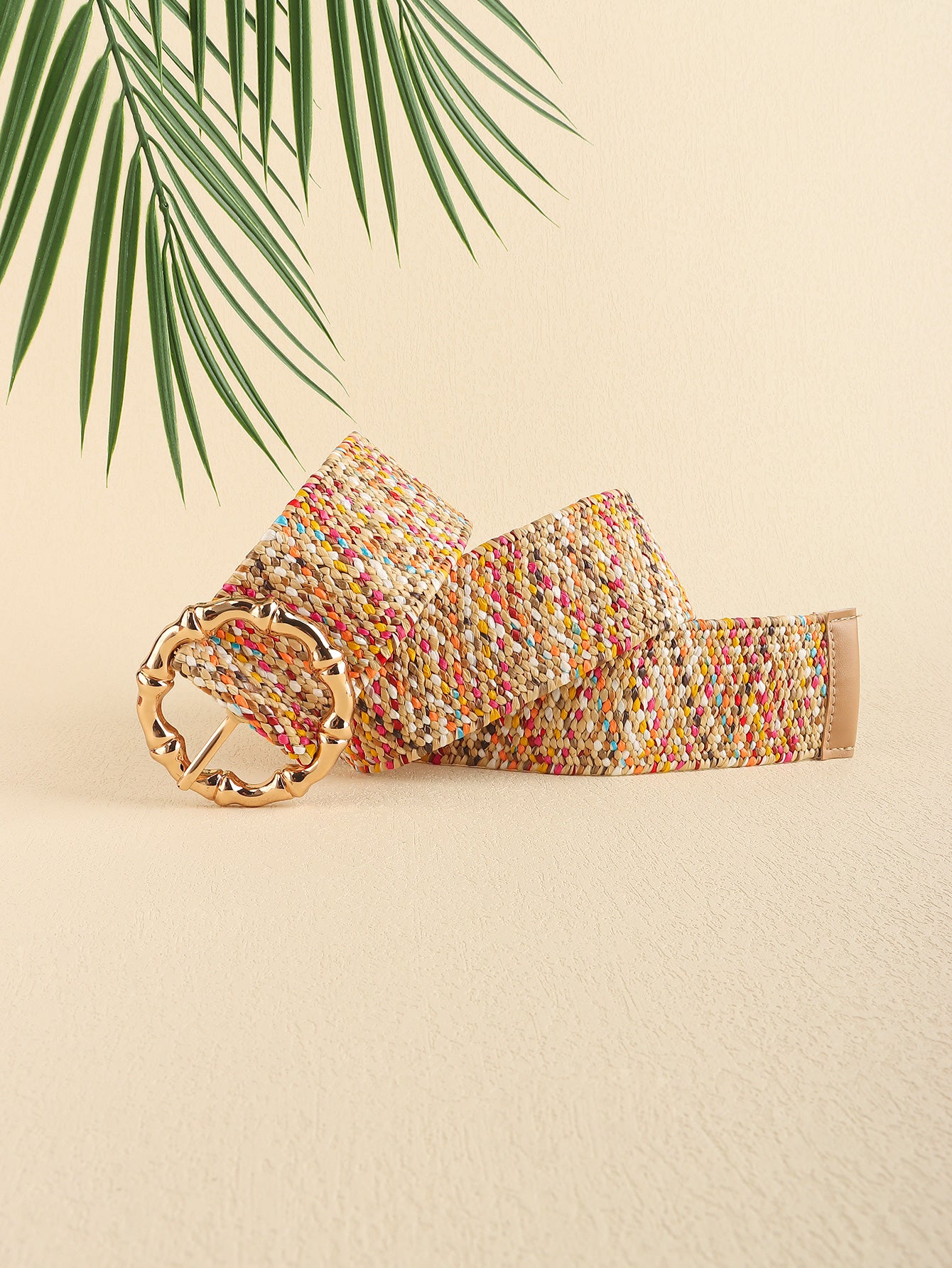 Multicolored woven belt with a gold buckle on a beige background with palm leaves.