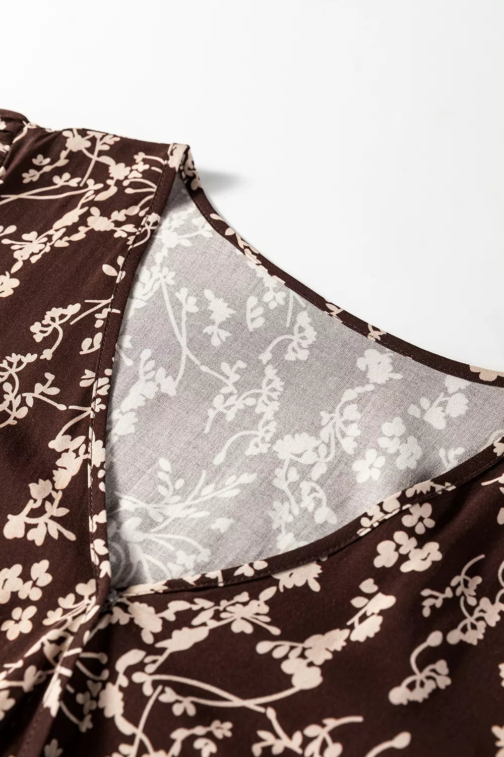 Close-up of a brown floral dress with a sheer overlay on a white background