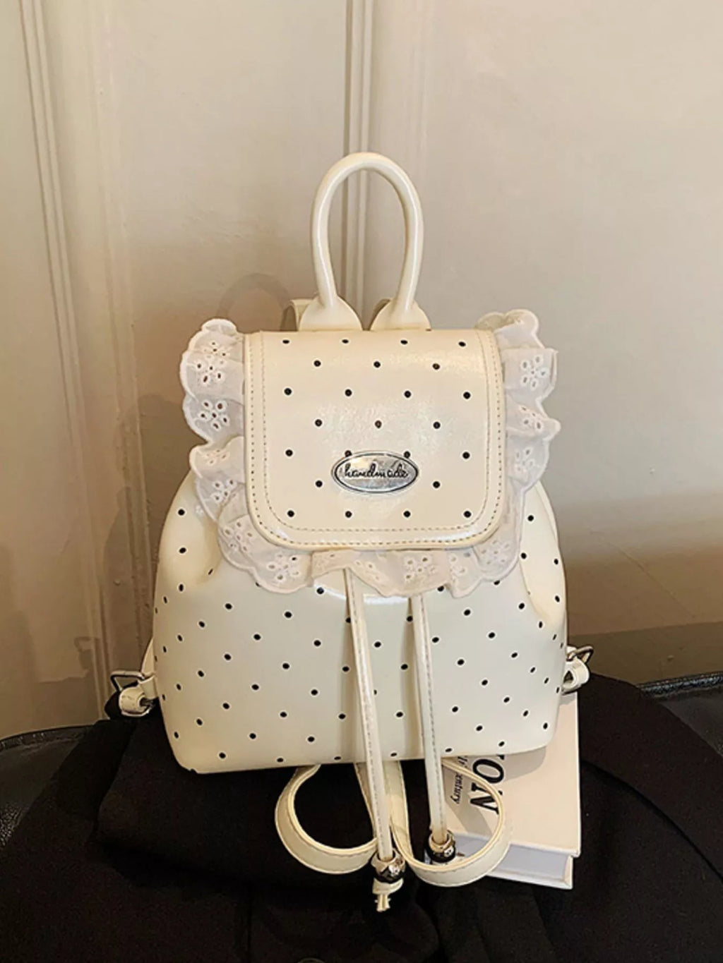 White polka dot backpack with lace details on a black surface