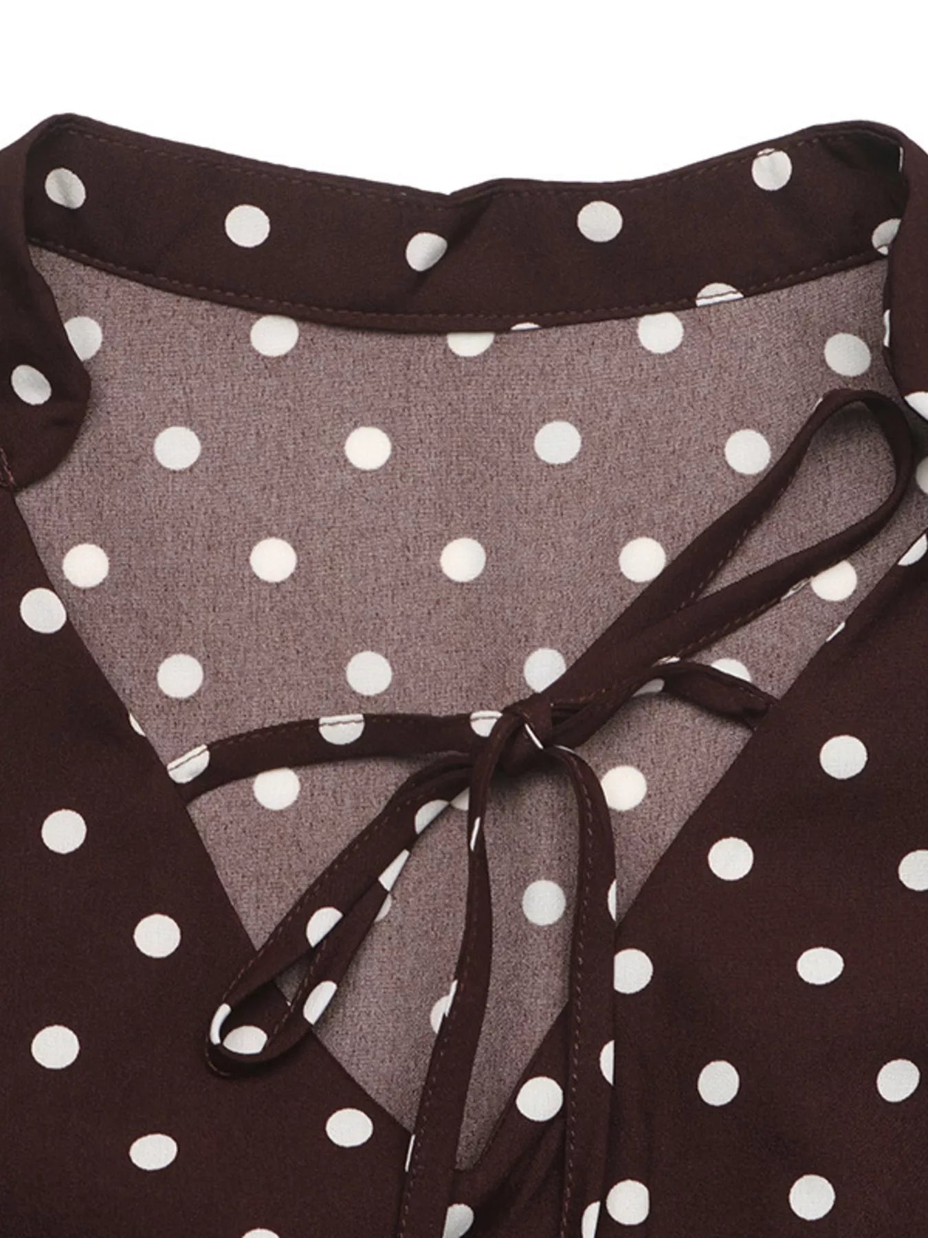 Close-up of a dark brown and white polka dot top with a ruffled neckline and tie detail.