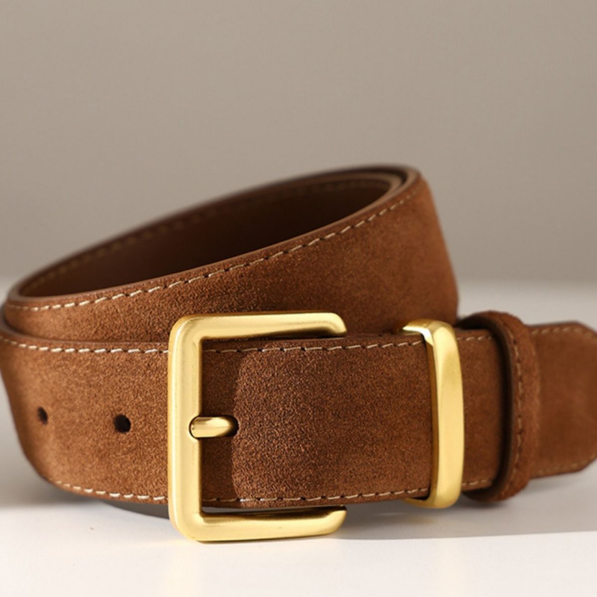 Brown leather belt with a gold buckle on a neutral background