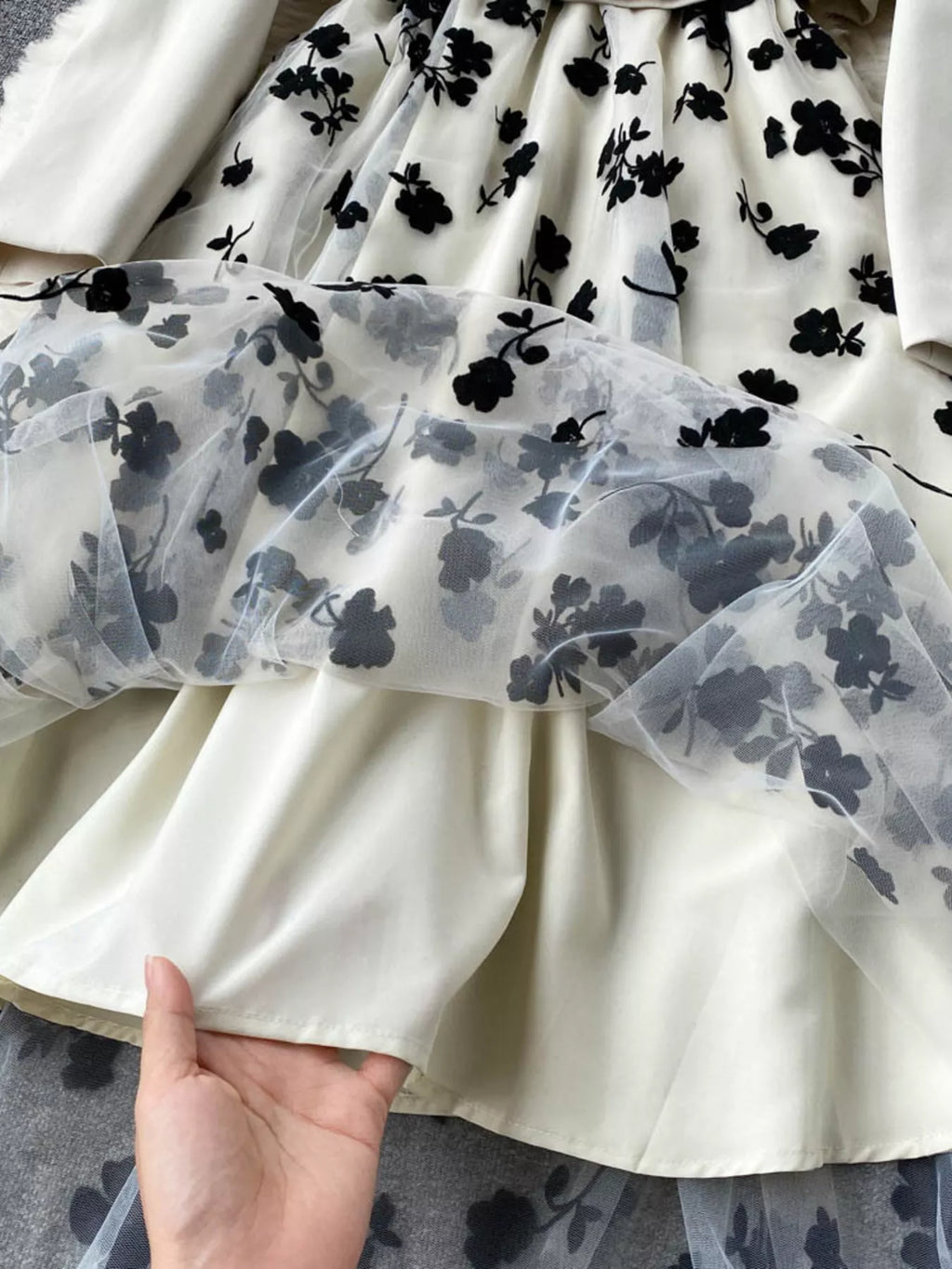 White dress with black floral pattern held by a hand on a gray surface