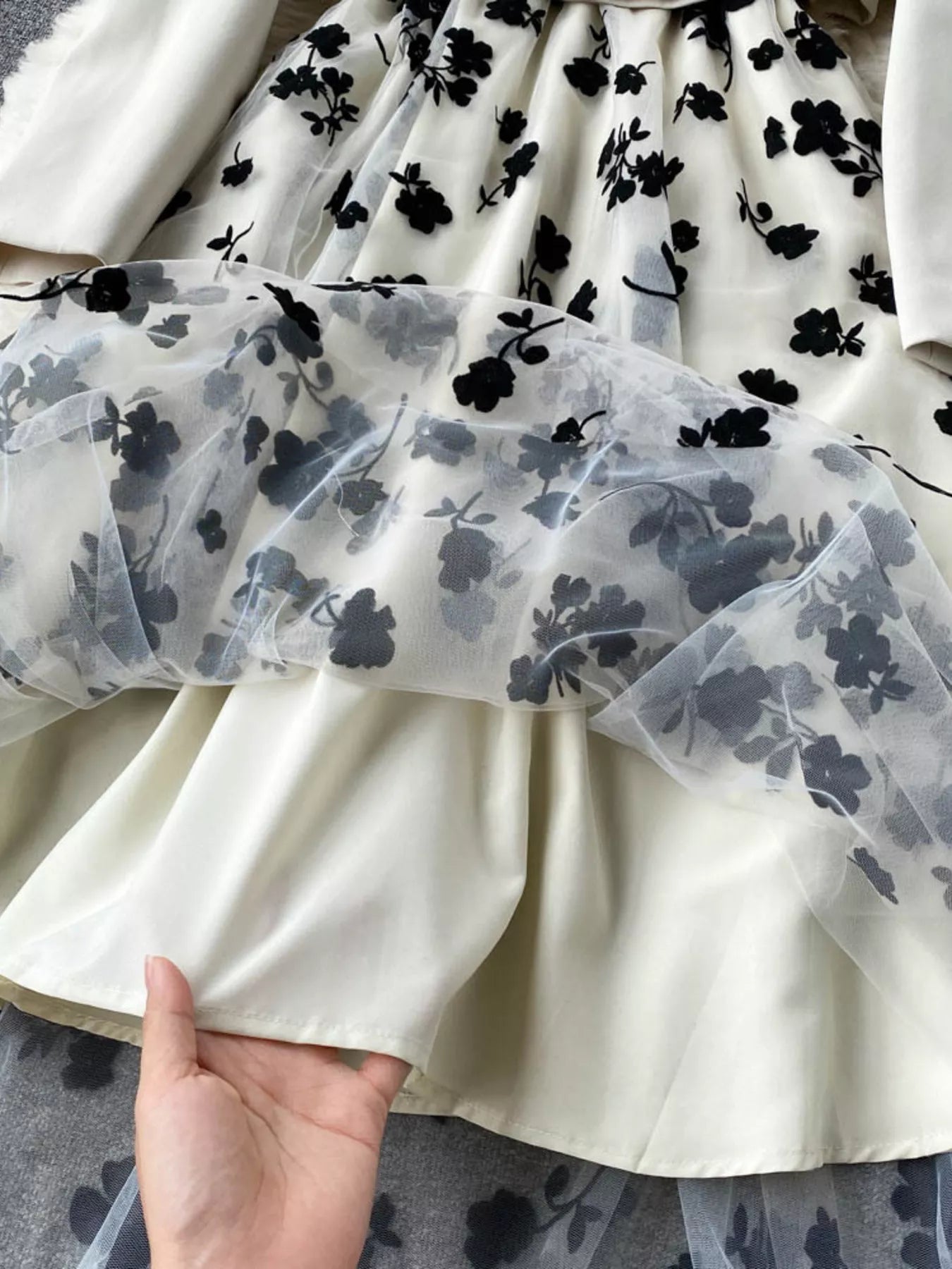 White dress with black floral pattern held by a hand on a gray surface