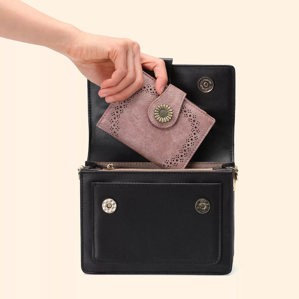 Black handbag with a pink wallet being placed inside on a beige background