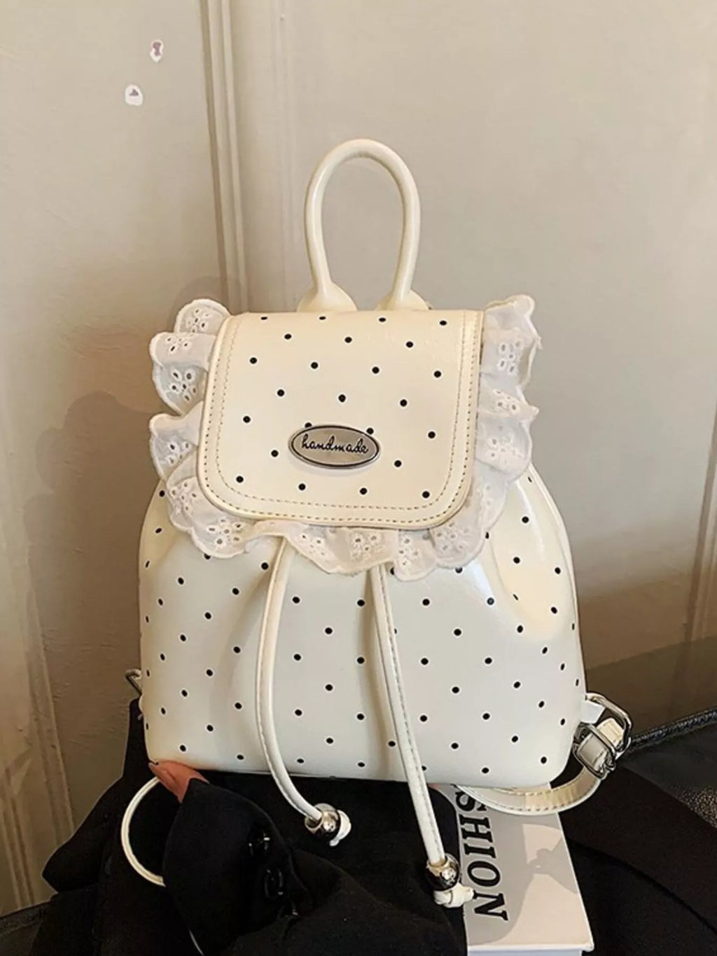 White polka dot backpack with lace details on a black surface