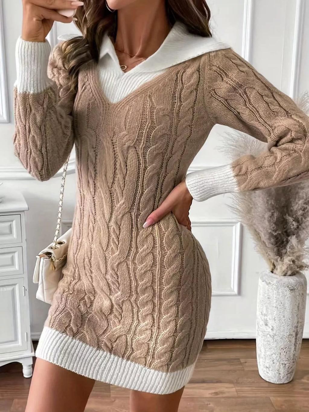 Woman wearing a beige cable knit sweater dress with white collar in a room.