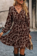 A woman wearing a long-sleeve brown wrap-style dress with a white floral print, standing outdoors on a cobblestone street.