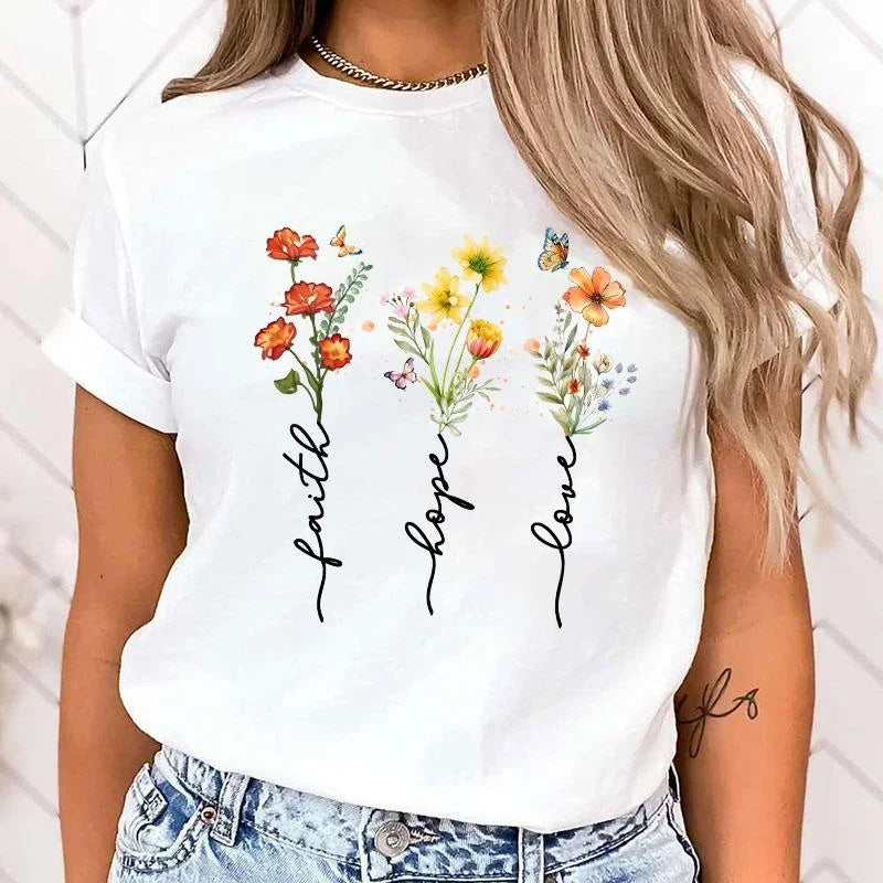 White t-shirt with floral designs and 'faith hope love' text worn by a person.