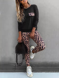 Person wearing a black sweatshirt with leopard print accents and leopard print pants, standing against a gray wall.