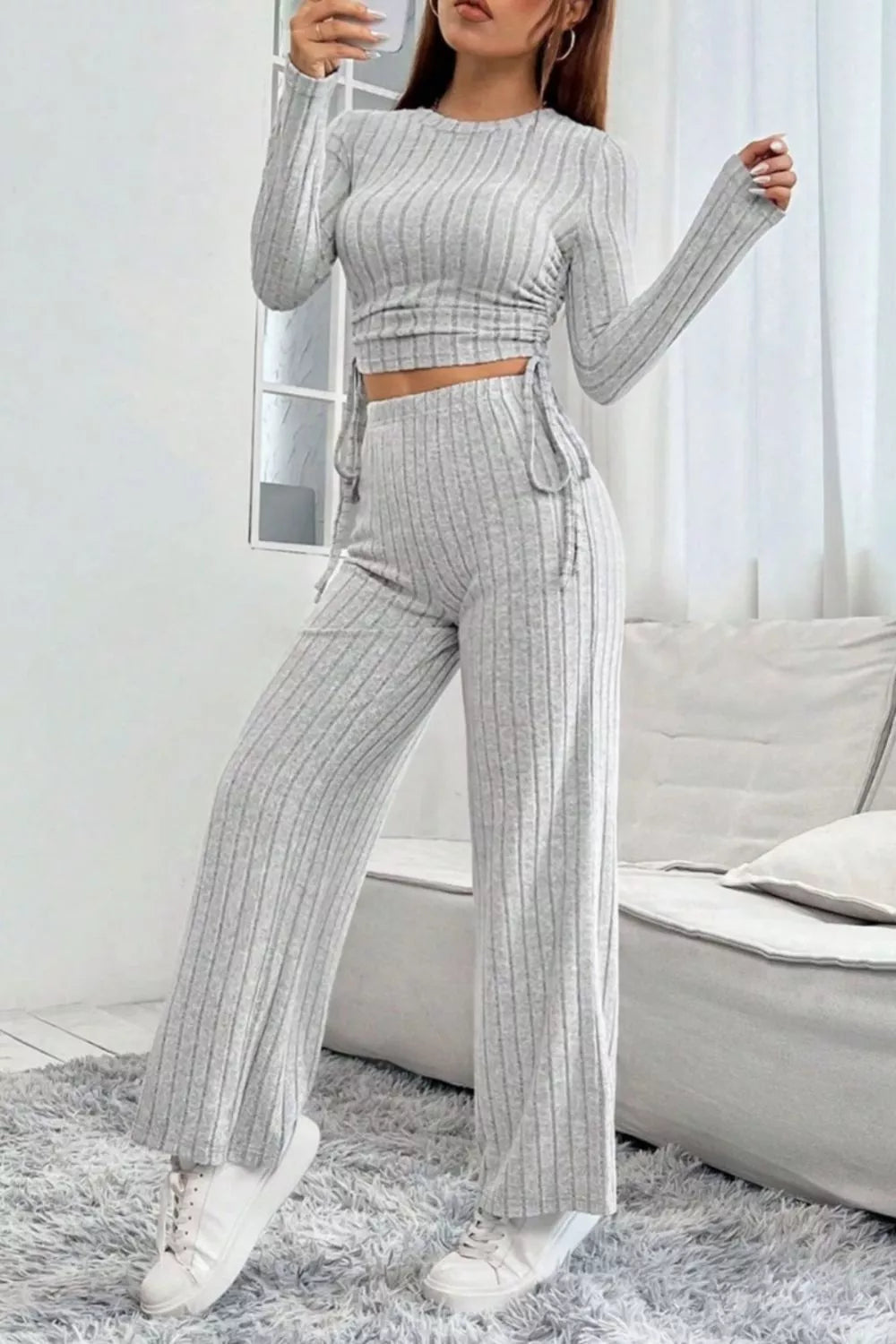 Woman wearing a gray ribbed outfit with matching pants and top in a minimalistic room.