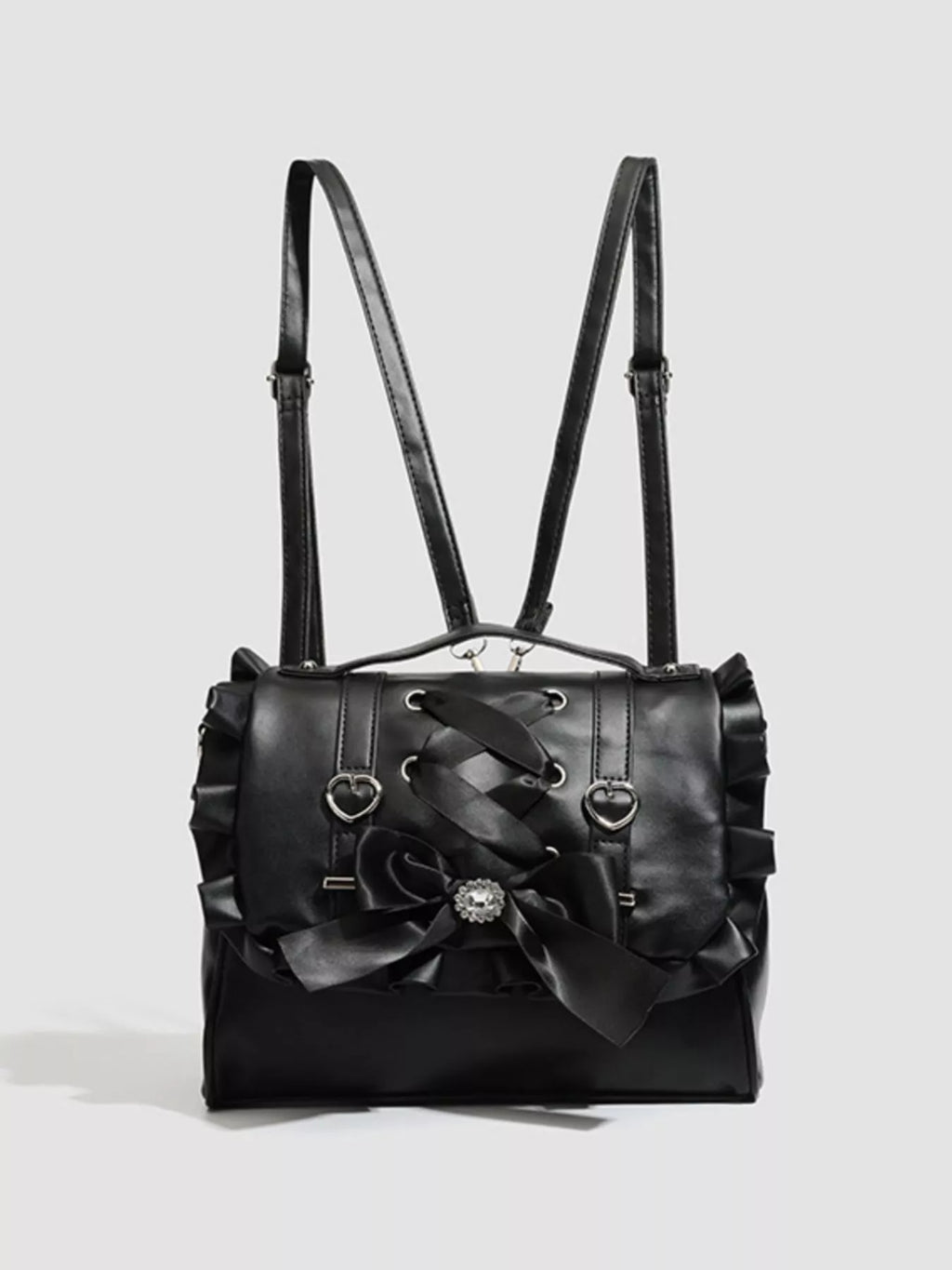 A black faux-leather shoulder bag with ruffled edges, dual shoulder straps, a large front bow, and heart-shaped metal details, shown on a light gray background.