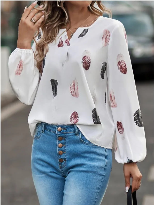 Woman wearing a white blouse with feather pattern and blue jeans outdoors.