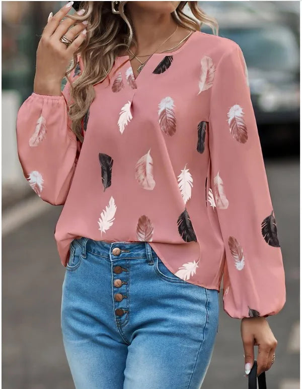 Person wearing a pink blouse with feather pattern and blue jeans on a blurred street background