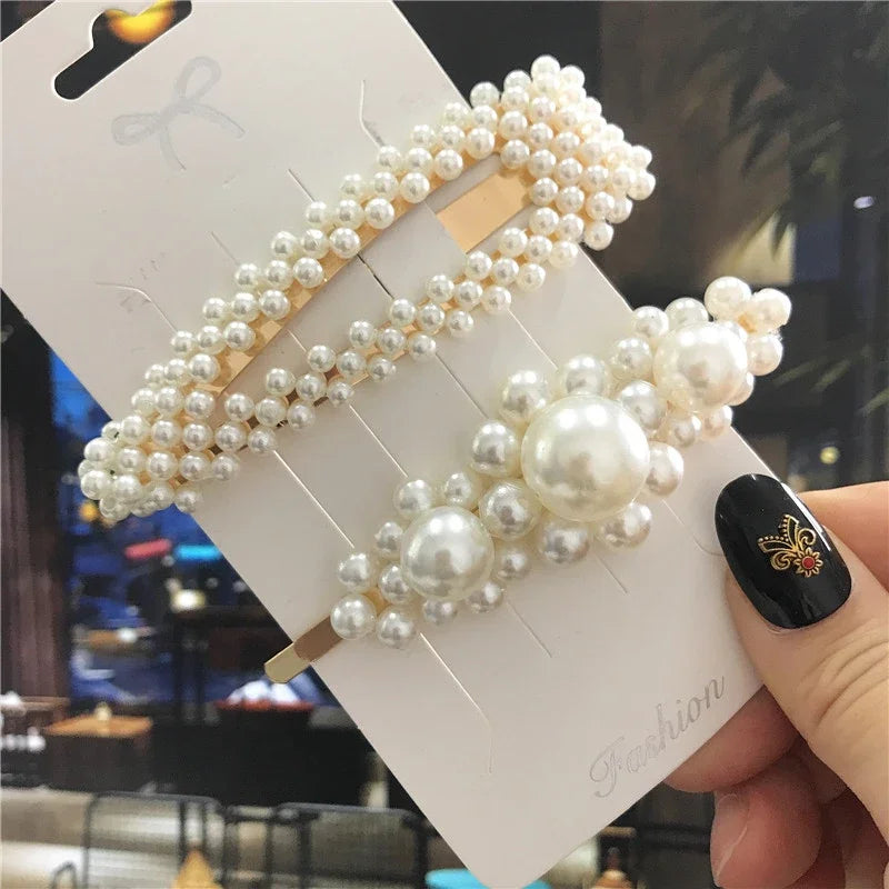 Pearl hair clips on a card held by a hand with black nail polish.