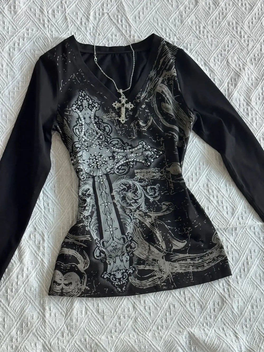 Black long-sleeve top with intricate white design on a textured white background