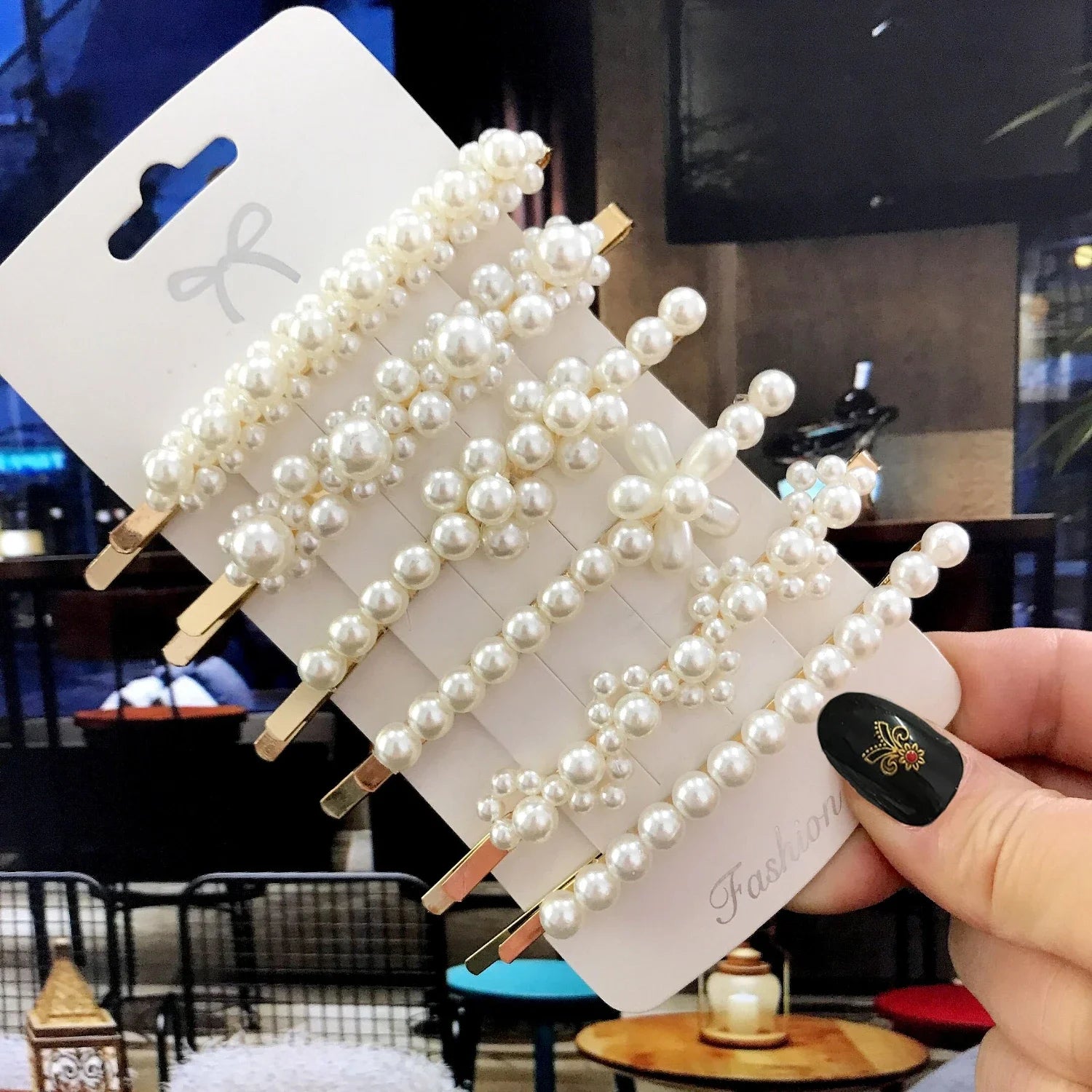 Pearl hair clips on a card held by a hand with a blurred indoor background