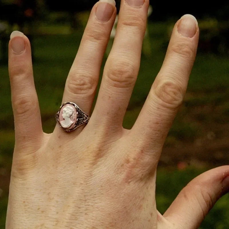 Hand wearing a ring with a visible stone against a blurred natural background