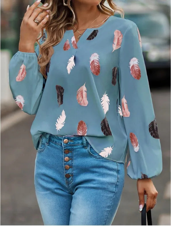 Woman wearing a blue blouse with feather pattern and blue jeans outdoors.