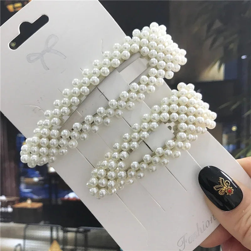 Pearl hair accessories on a white card held by a hand with black nail polish.