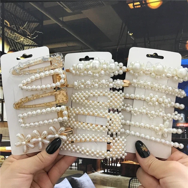 Three packages of pearl hair clips held by a person with a blurred indoor background.