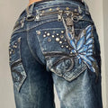 Blue jeans with decorative elements including a butterfly patch, studs, and chains on a plain background.