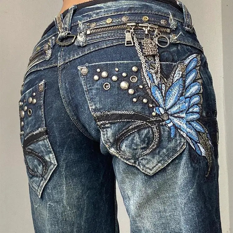 Blue jeans with decorative elements including a butterfly patch, studs, and chains on a plain background.