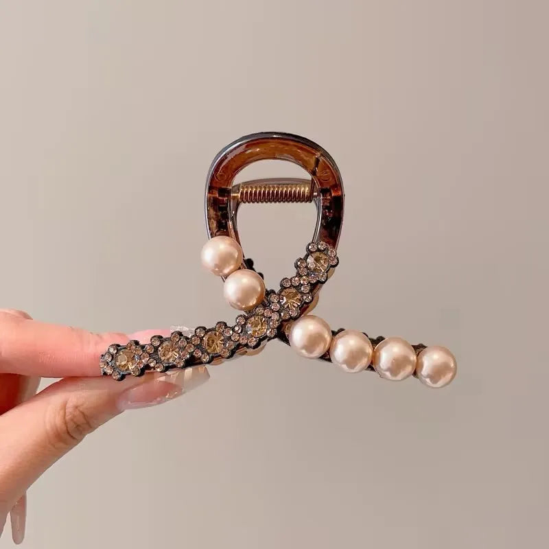 Hair clip with pearls and tortoiseshell design held by a hand against a neutral background