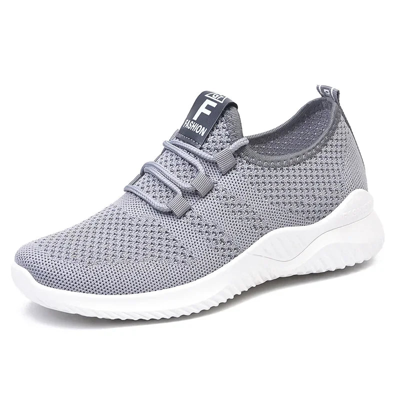 A gray knit athletic sneaker with a white sole, featuring a black tongue label with white text that reads 'FEEL FASHION'.
