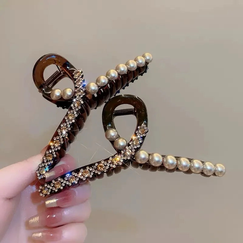 Hair clip with pearls and rhinestones held by a hand against a neutral background