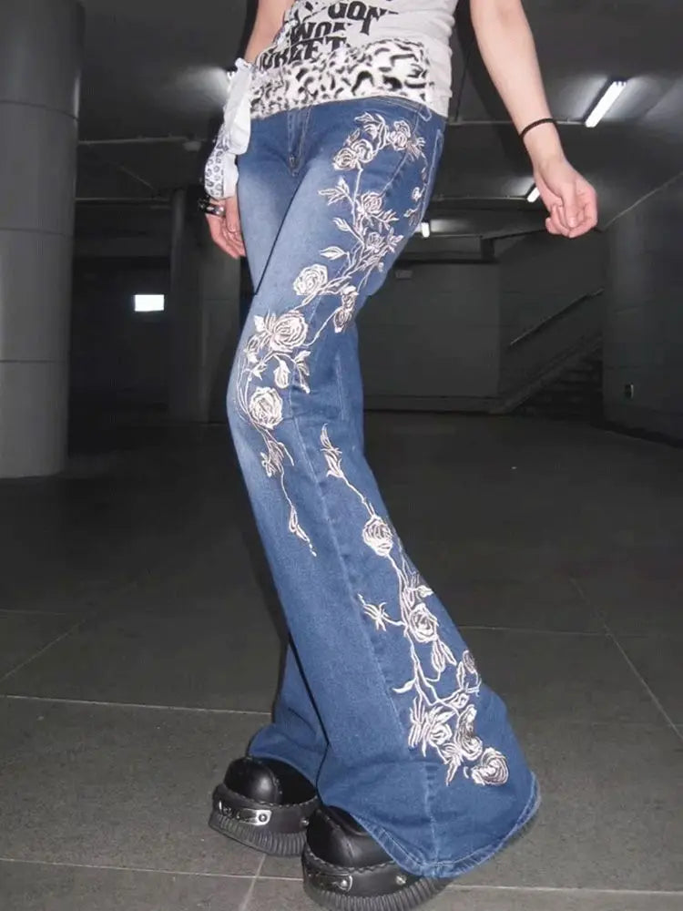 Model wearing blue jeans with floral embroidery in a dark indoor setting