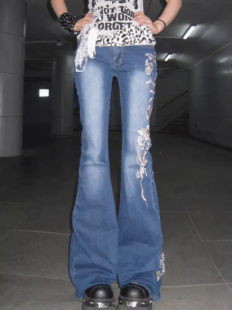Model wearing blue flared jeans with floral embroidery in a dark indoor setting