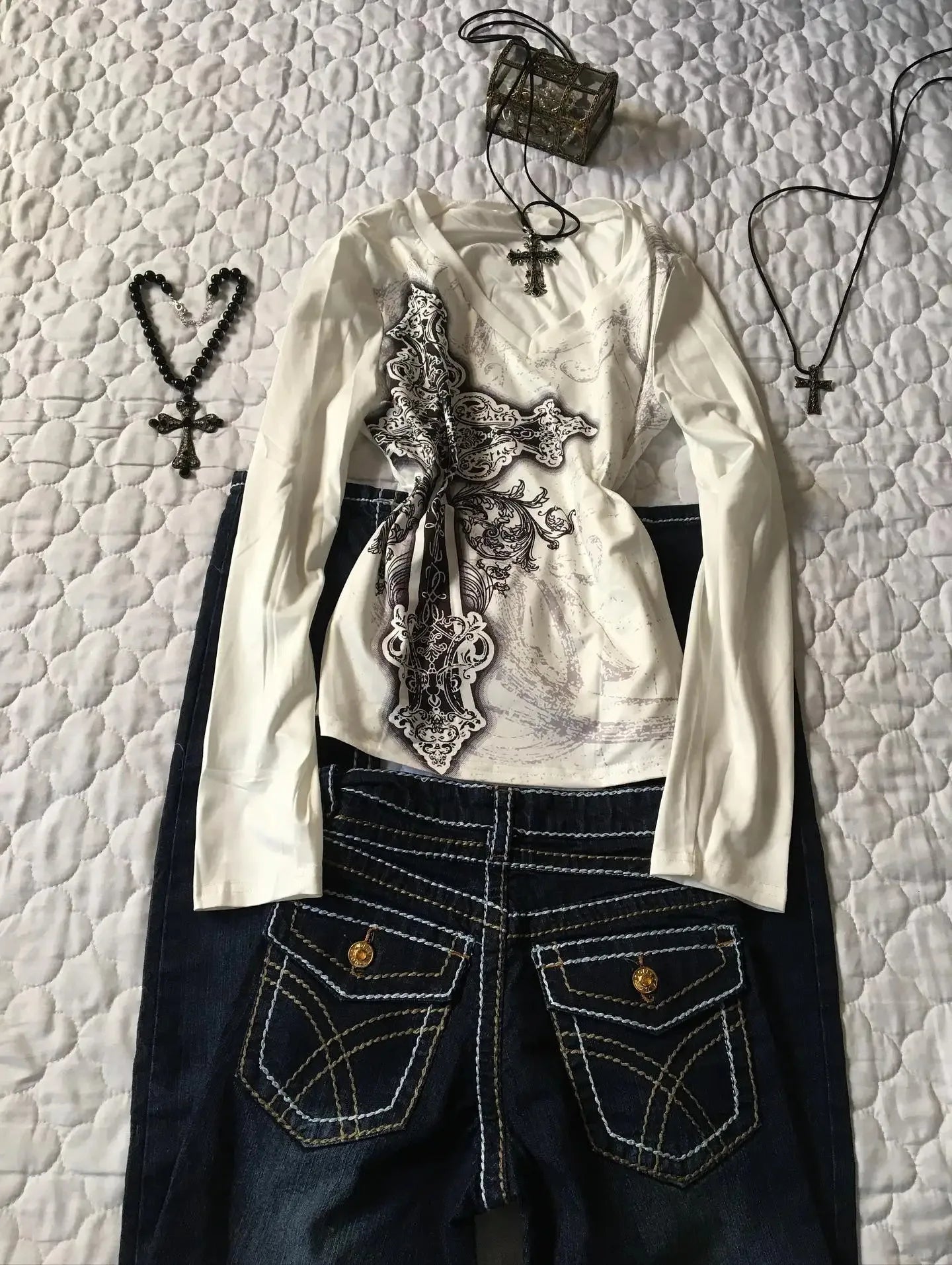 White blouse with lace details and dark jeans on a textured white background