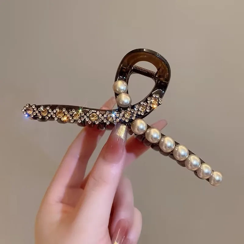 Hand holding a decorative hair clip with pearls and crystals against a neutral background
