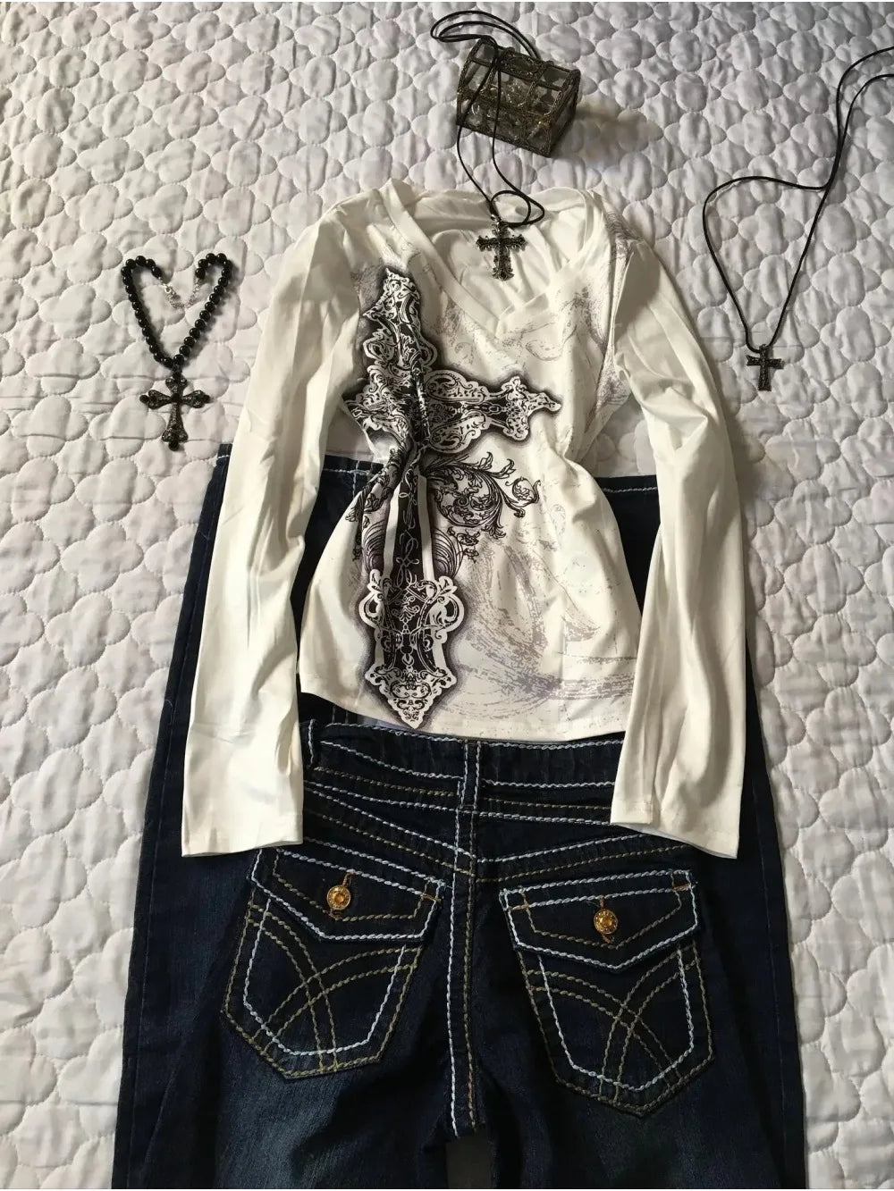 White blouse with lace details and dark jeans on a textured white background