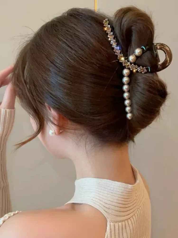 Woman with a stylish hair bun adorned with pearls and beads against a neutral background