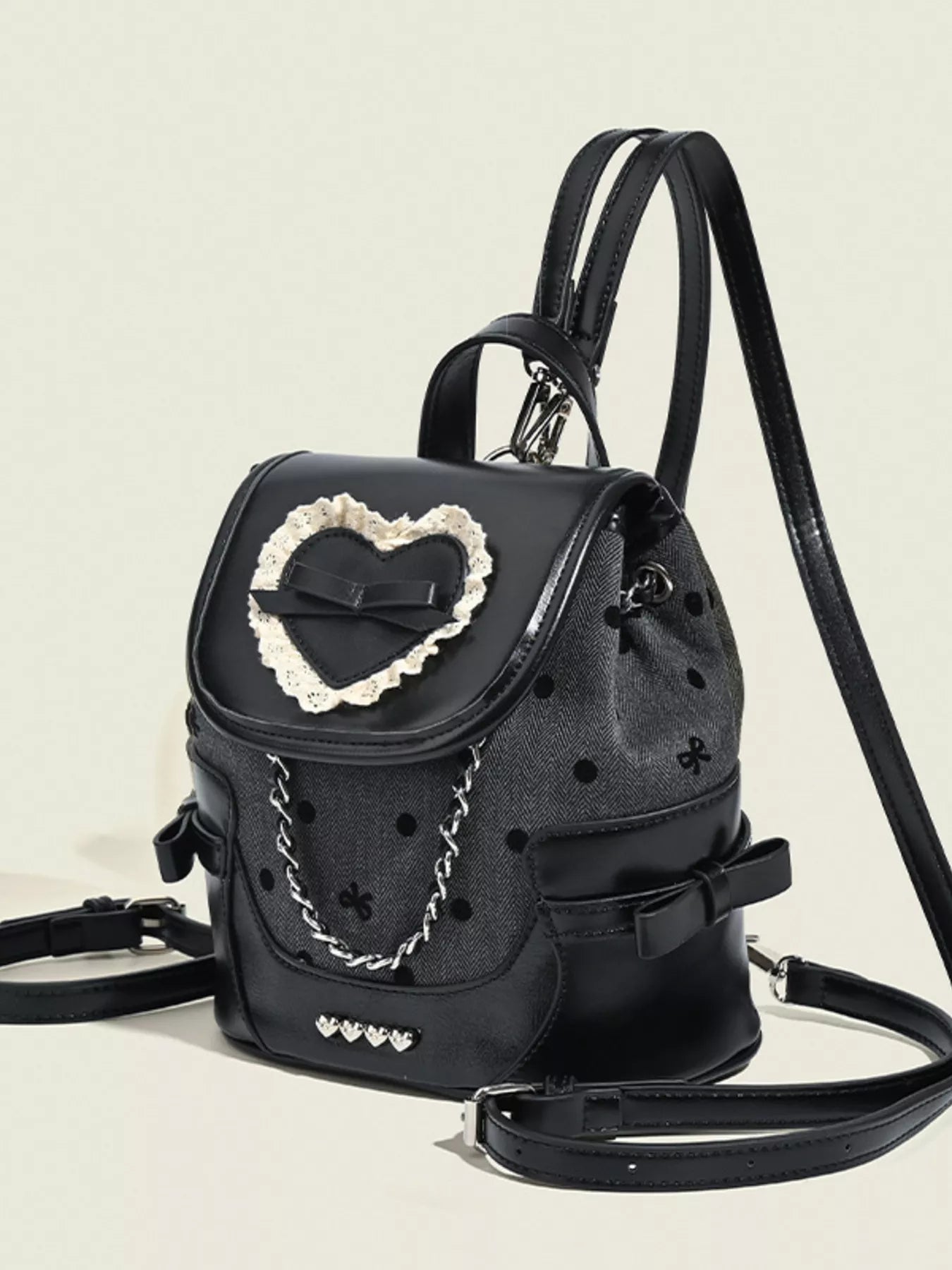Black backpack with decorative heart and chain detail on a beige background