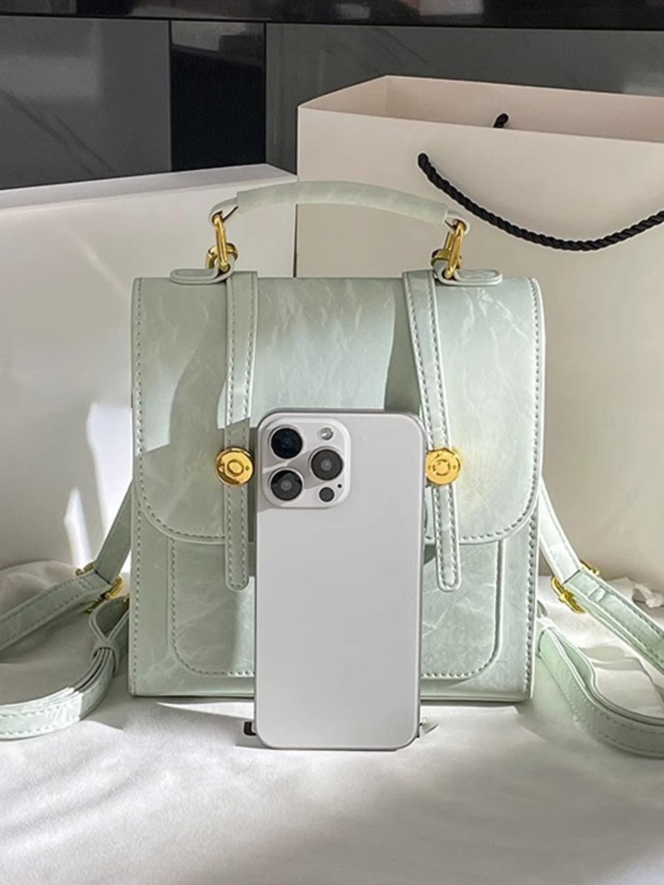 Light green handbag with gold accents and a phone on a white surface