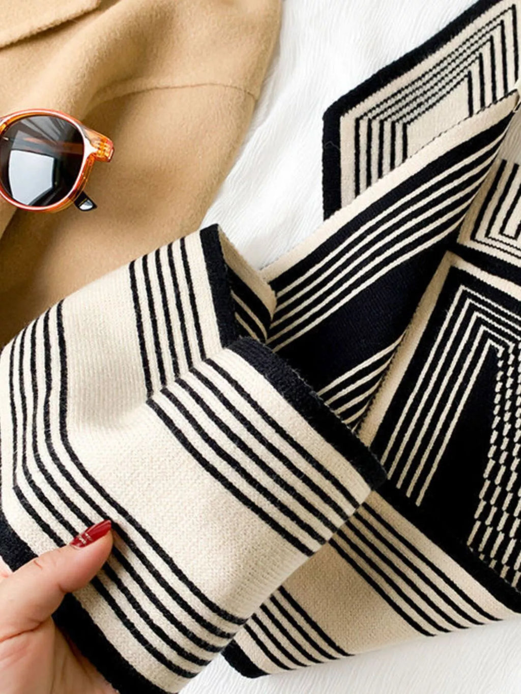 A black and white patterned scarf with sunglasses and a coat in the background