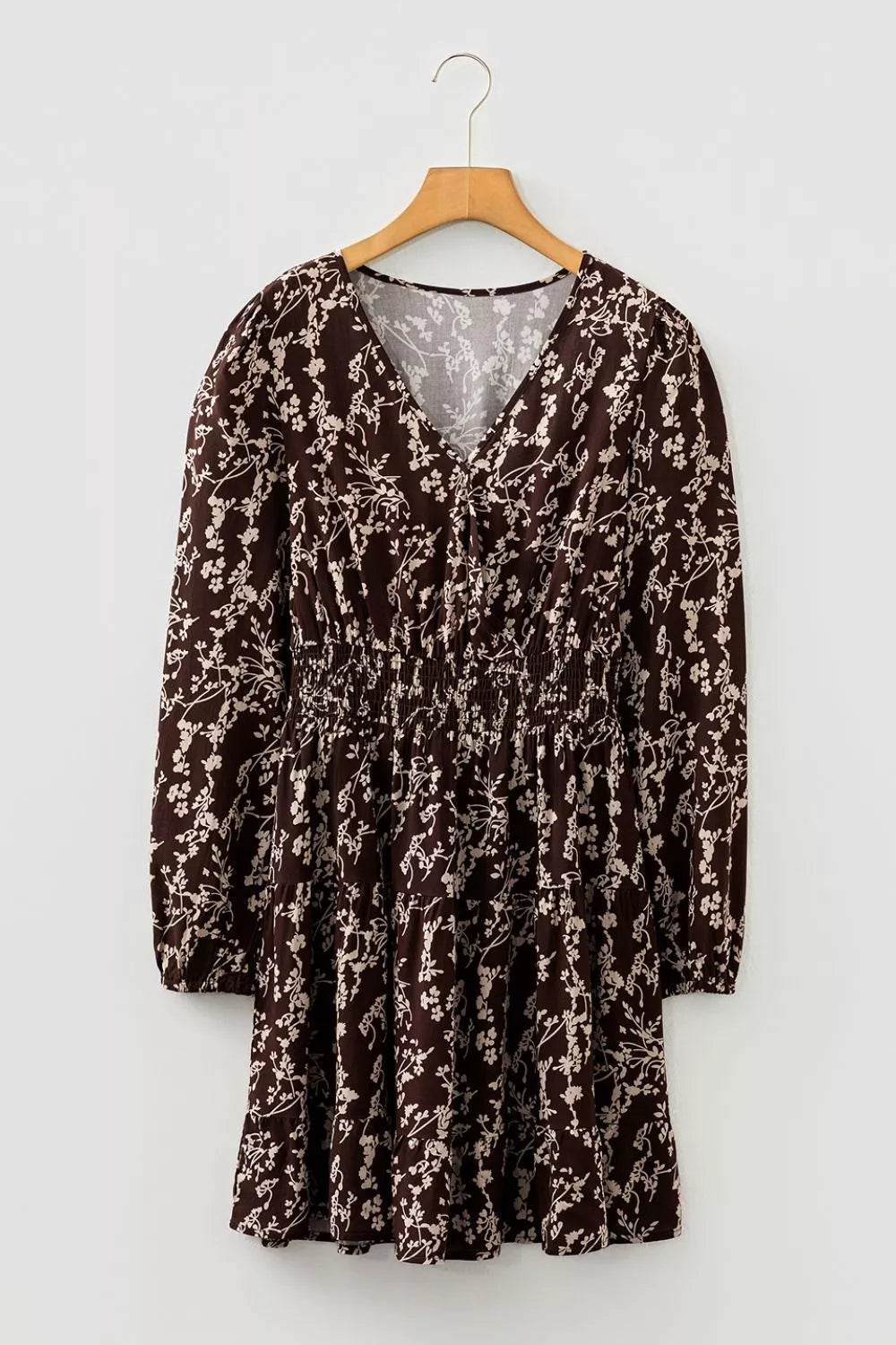 A long-sleeve V-neck dress with an all-over floral print in dark brown and beige, hanging on a wooden hanger against a light gray background.