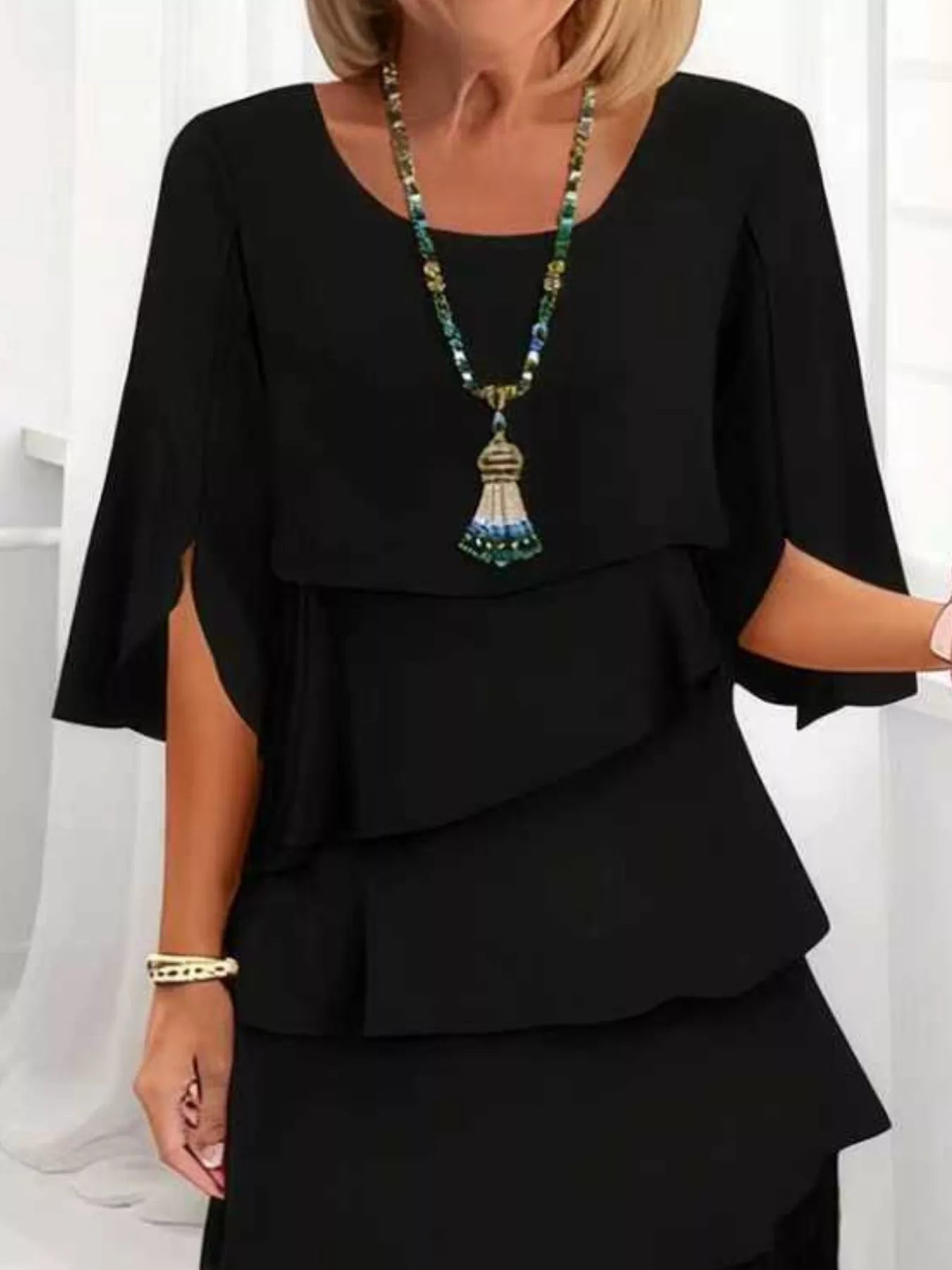 Woman wearing a black outfit with a long necklace against a white background