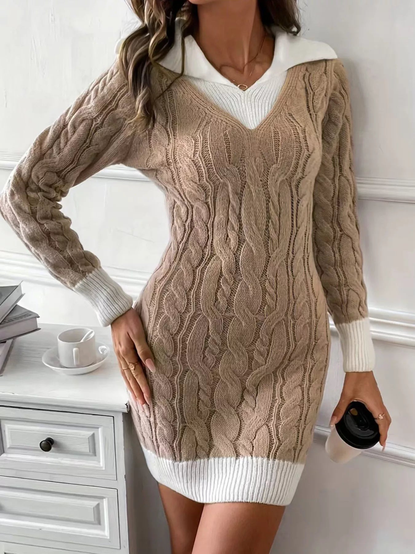 Beige cable knit sweater dress worn by a person in a home setting.