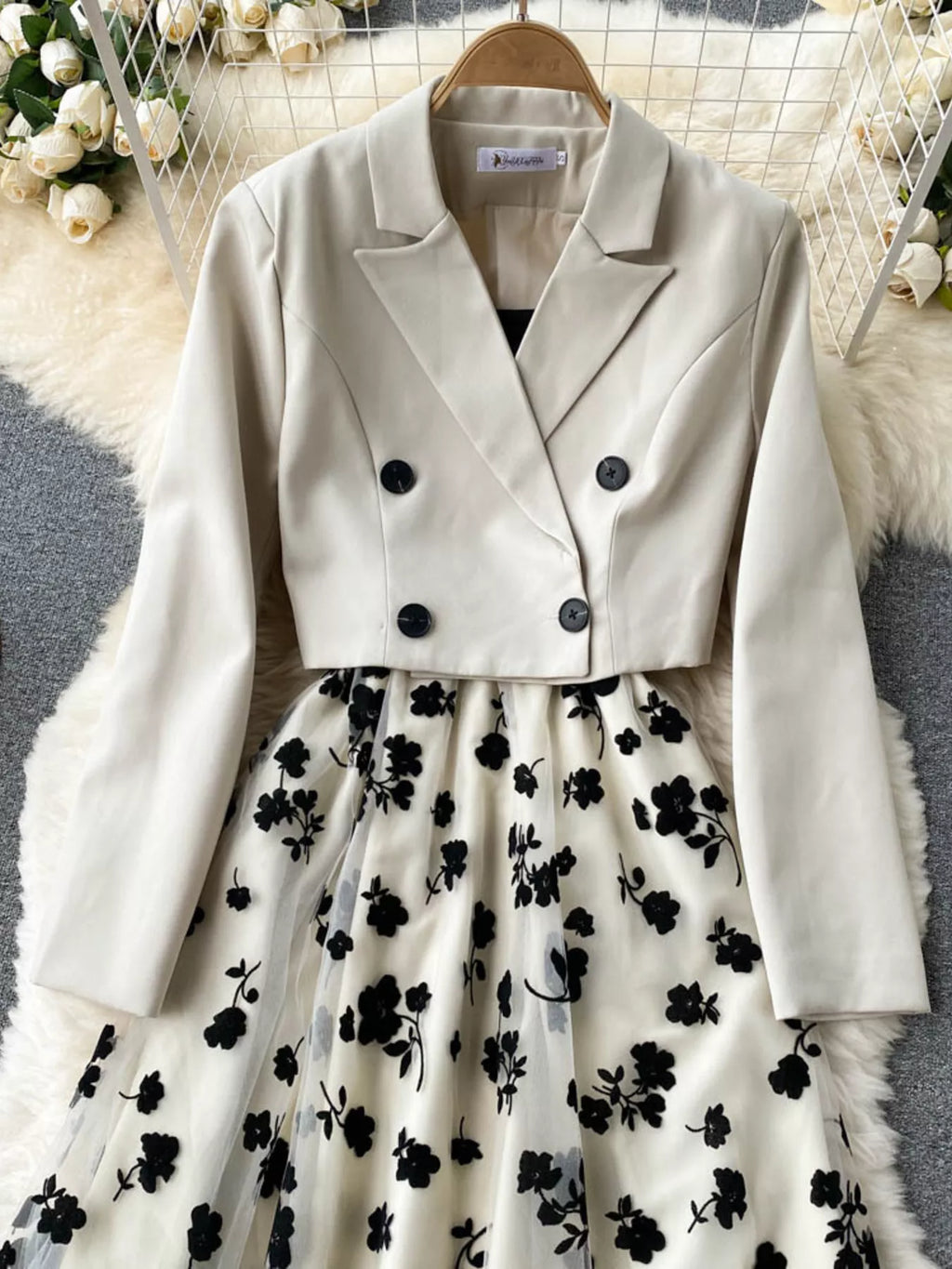 White blazer over a black floral dress on a hanger with a soft white background