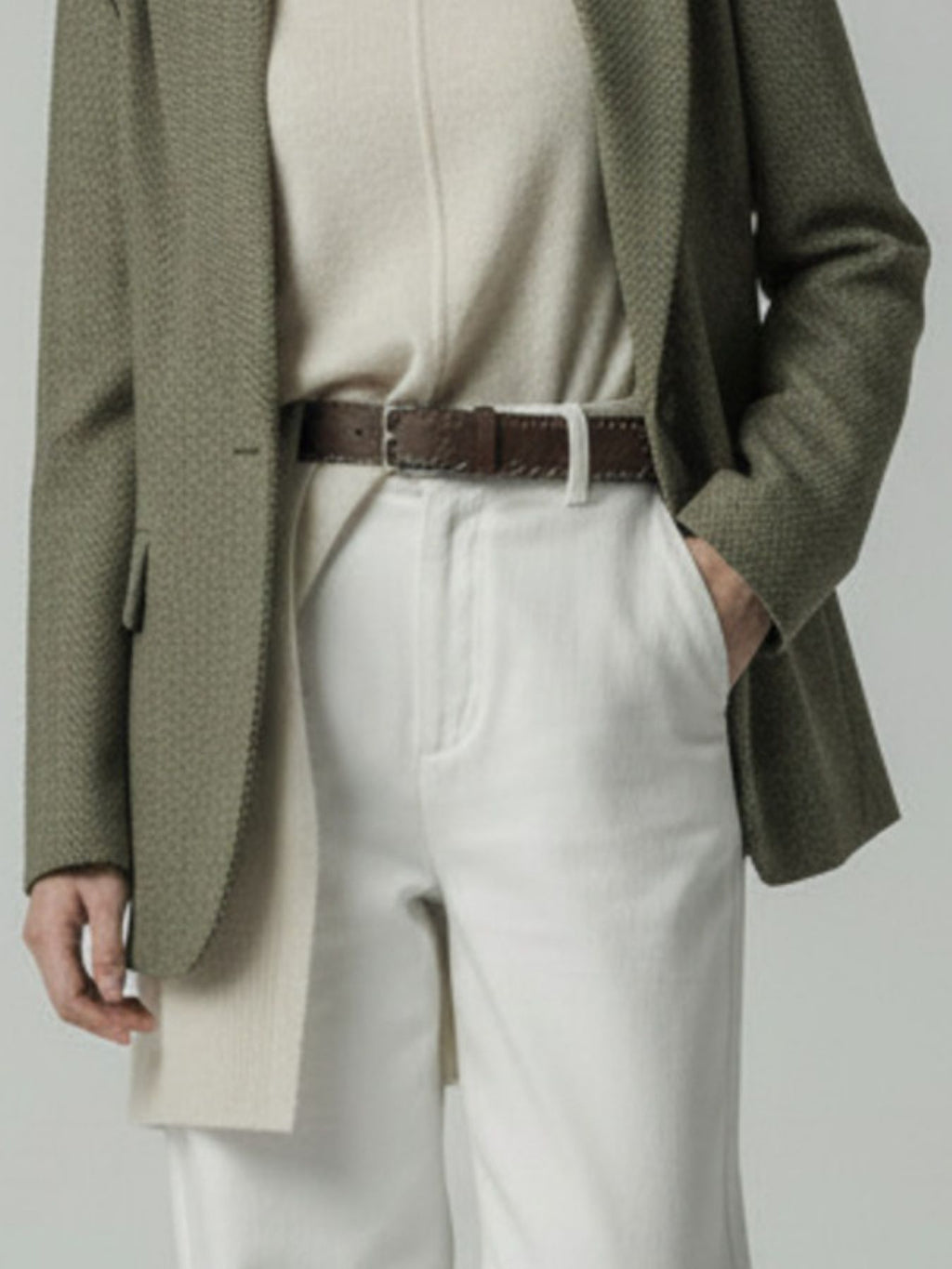 Model wearing a green blazer, beige sweater, and white pants with a brown belt.